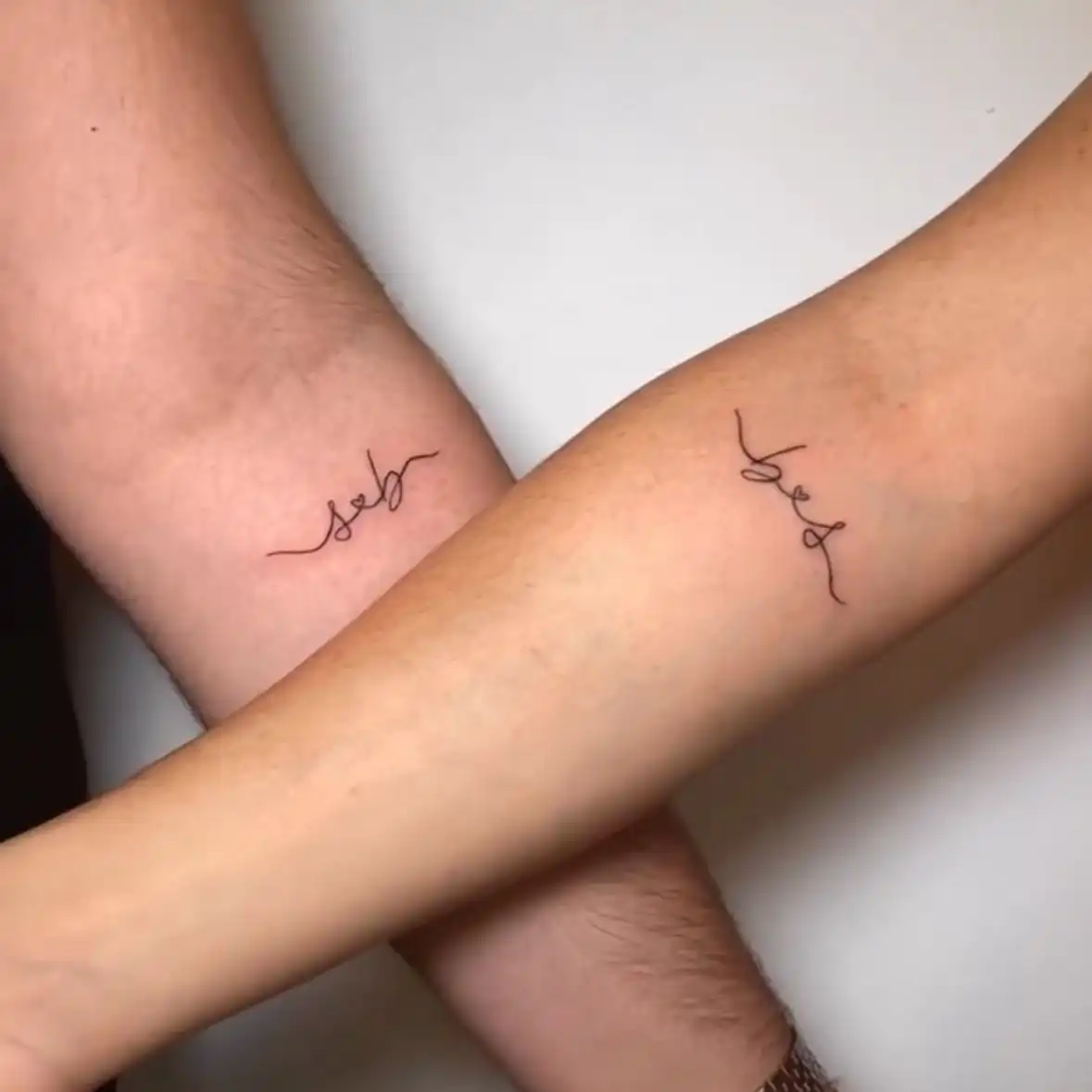 Dos tatuajes de lettering fino a juego en los brazos